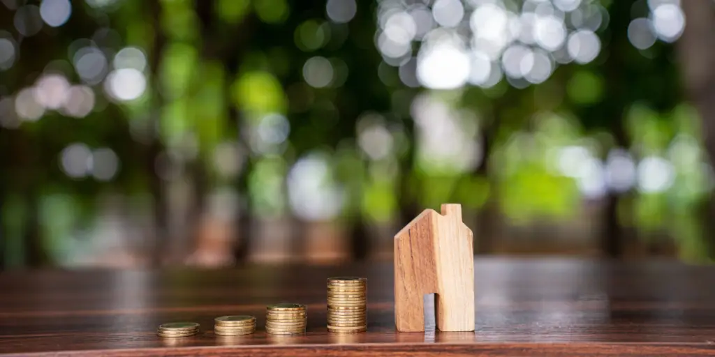 Small wooden home with increasing stacks of coins, indicating increase in value.